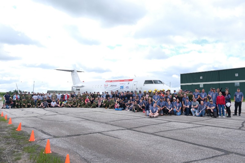 A large group of people gathering in front of an aircraft. The group includes individuals in military uniforms and civil clothing, for a collaborative event associated with an aviation and community event.